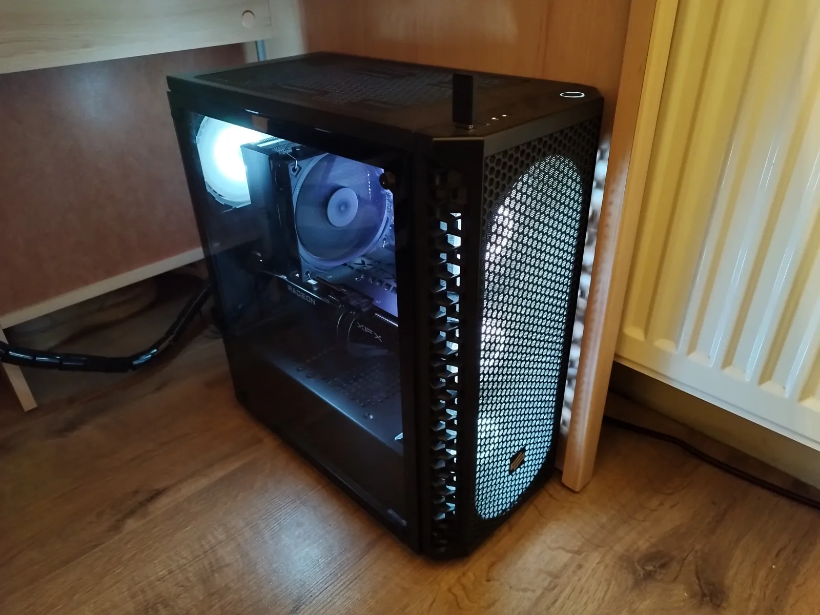 The main PC: a black mid-tower with a tempered-glass side panel and mesh front, white-lit fans, with the Fera 5 cooler and XFX Radeon card visible inside.